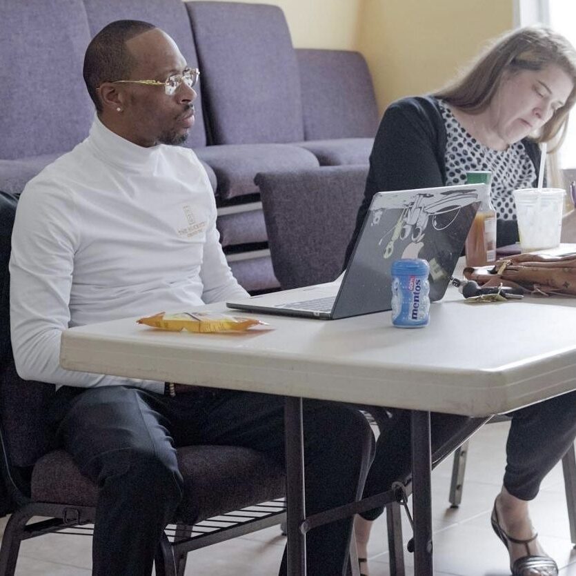 Two people sitting at a table with laptops.